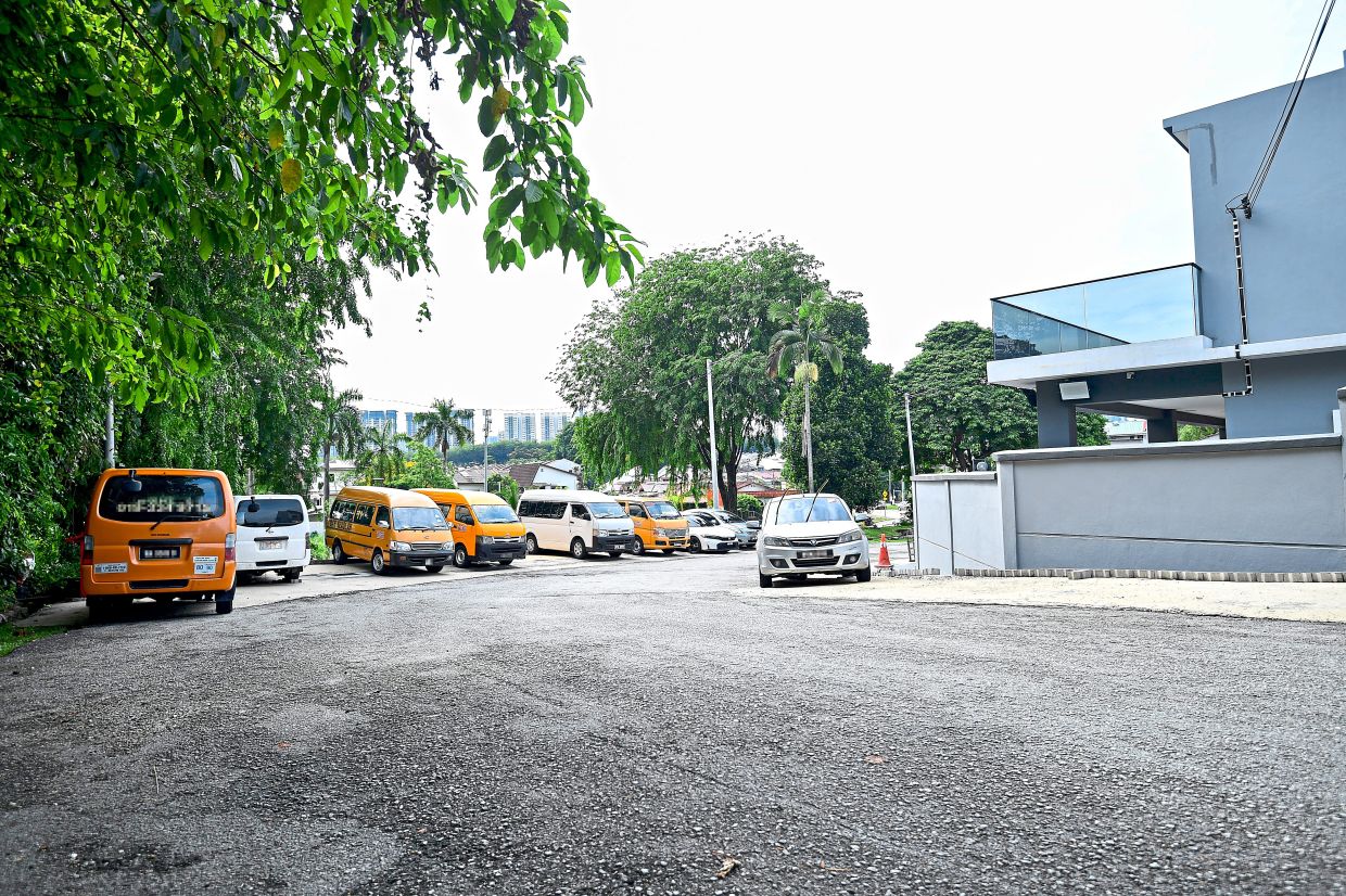 School buses and vans among other vehicles parked along a bend in Jalan Nyaman 11, Taman Bukit Indah.