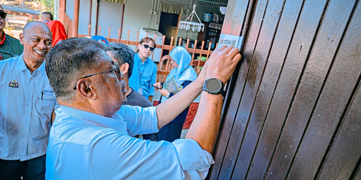 Ab Rauf places a QR-coded address on a Melaka home. Kampung Digital gives traditional village homes standardised digital addresses with key location details.