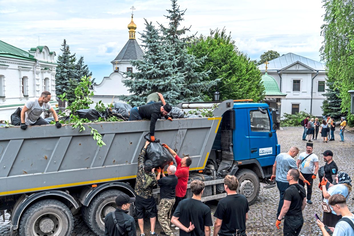 People loading bags of leaves and branches into a dump truck while cleaning the grounds of the Kyiv-Pechersk Lavra.