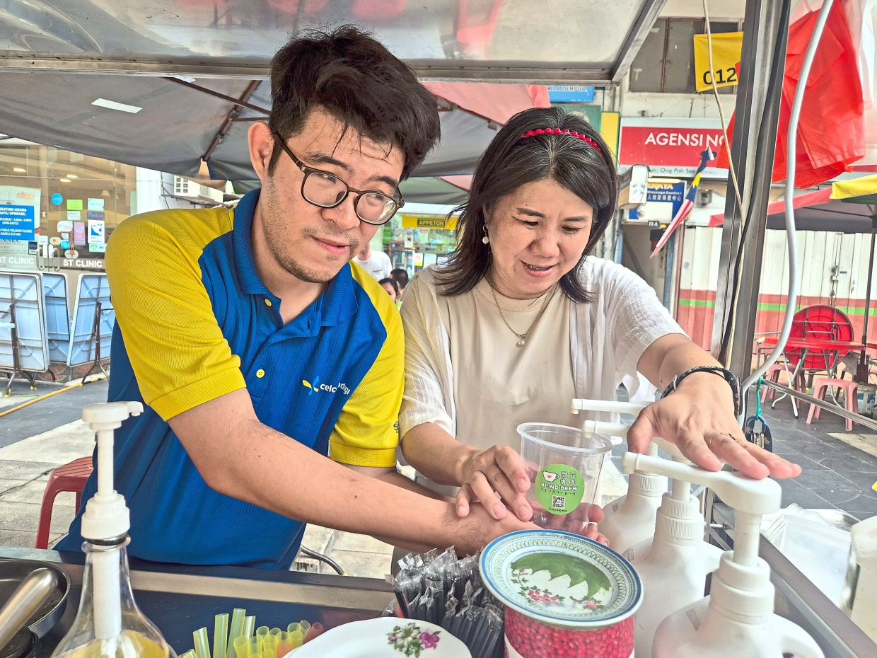 Chew (right) guides Foo as he learns to manage the drink stall.