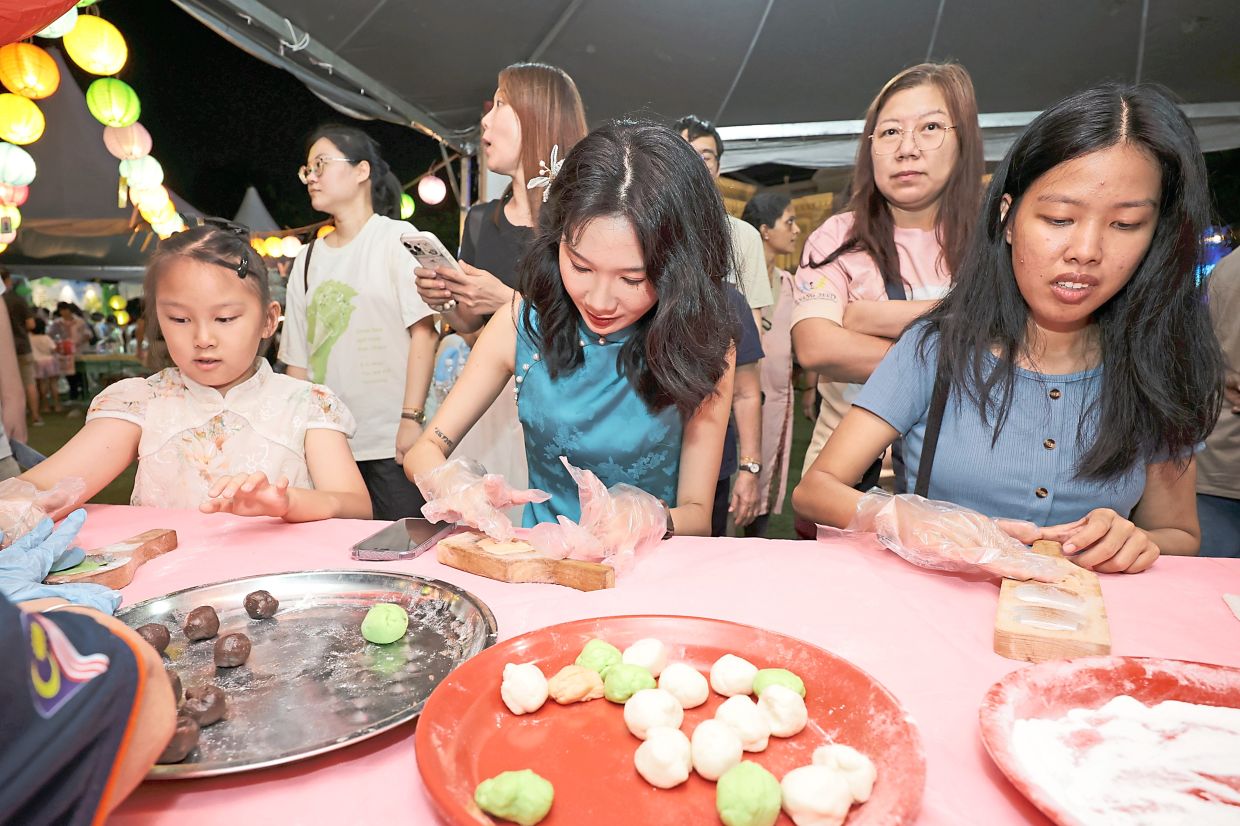 Hee (seated middle) and other visitors trying their hand at shaping dough, inserting fillings and pressing them into wooden moulds during a hands-on mooncake-making workshop.