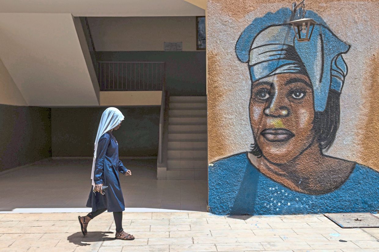 A student walks past a wall painting of Mariama Ba at the school. Photo: Caitlin Kelly/AP