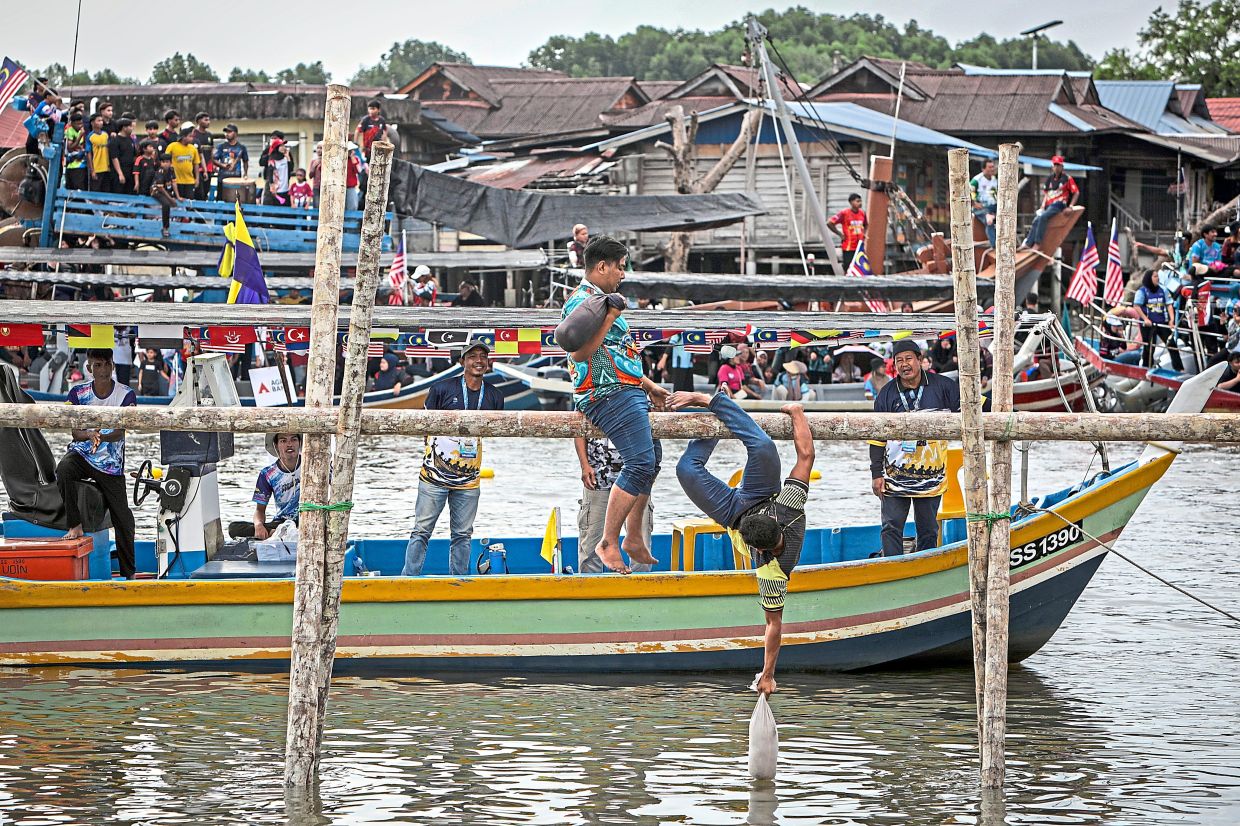 Participants of a water pillow fight trying to knock each other off a pole. 