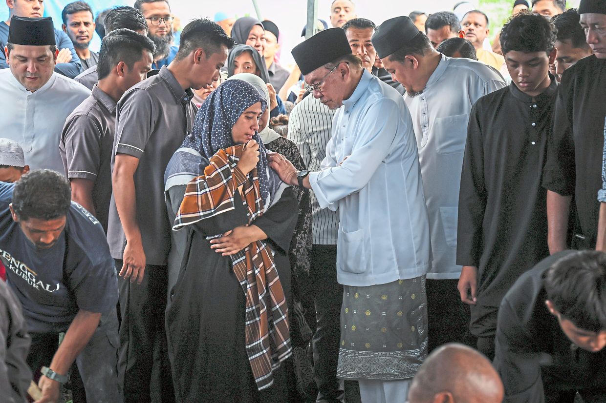 Stay strong: Anwar (centre) consoling his niece Aida Rabitah Idrus at the funeral of his late brother Idrus. — Bernama