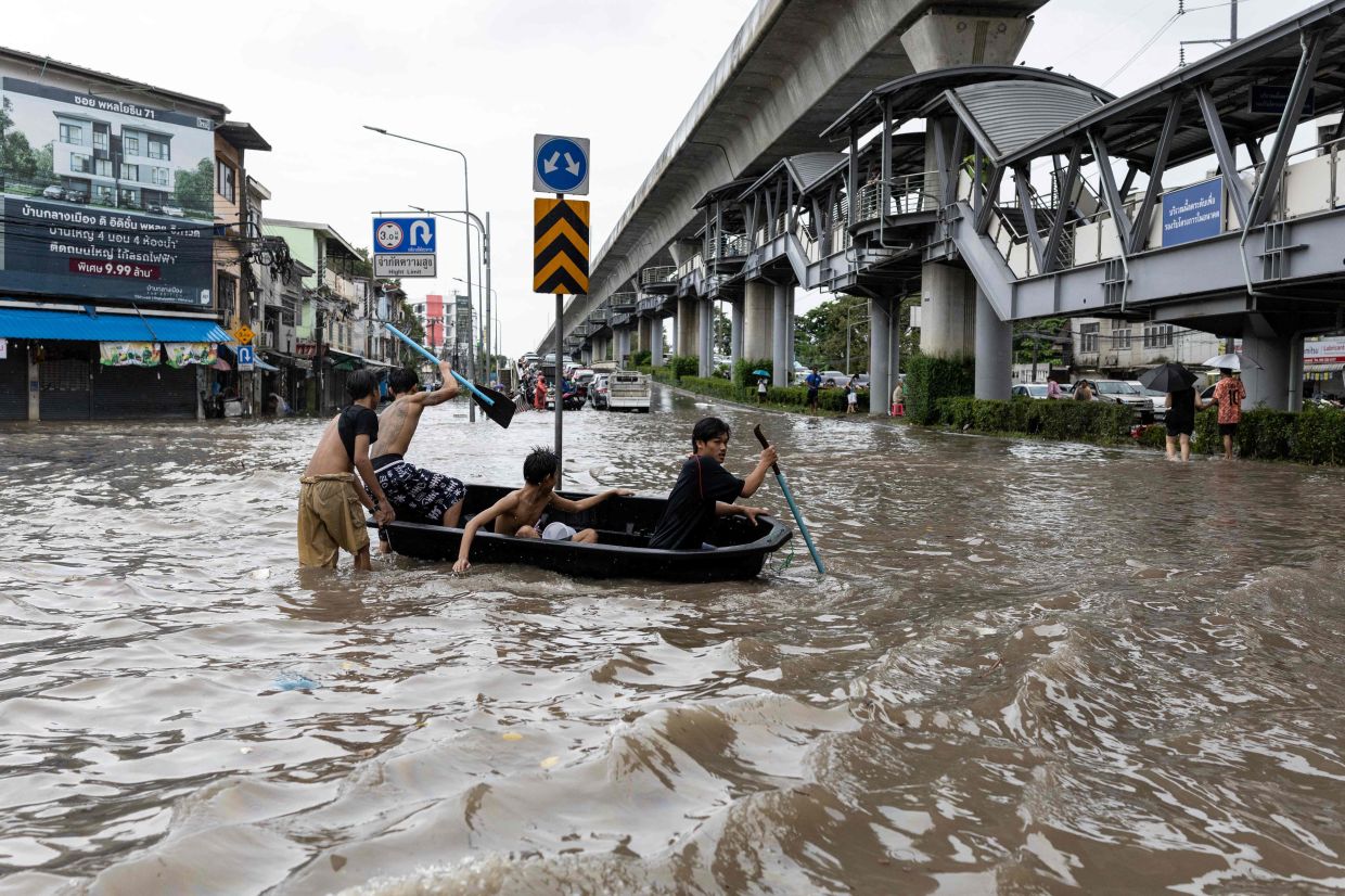 Young men navigate a small boat through floodwaters in the Bang Bua district of Bangkok on September 26, 2026. Bangkok authorities declared a flood disaster across the Thai capital after almost 48 hours of heavy rain left canals full, roads submerged and residents wading through deep water. - Photo: AFP