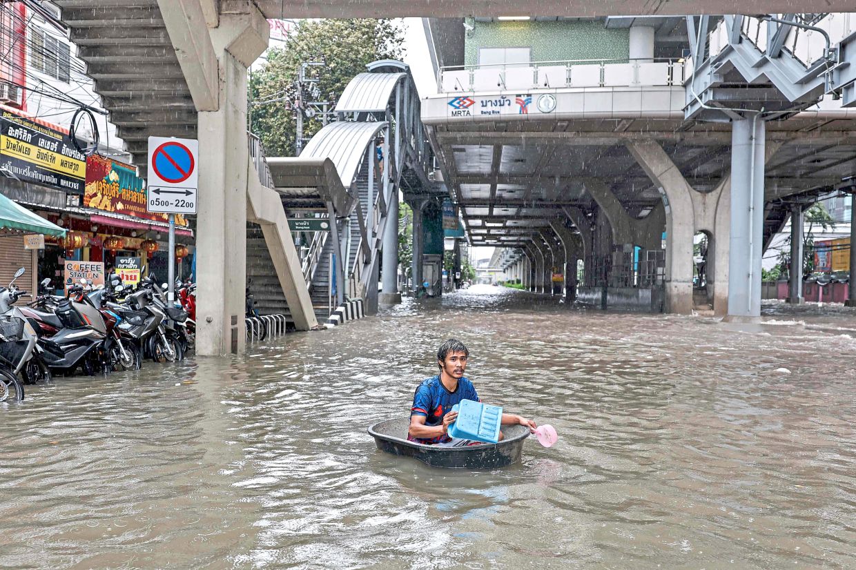 Roads turn into rivers: A man using a large plastic tube to wade through floodwaters in the Bang Bua district of Bangkok. (Below) A man taking pictures as people walk through waters along Phetchaburi Road in Bangkok. — AFP