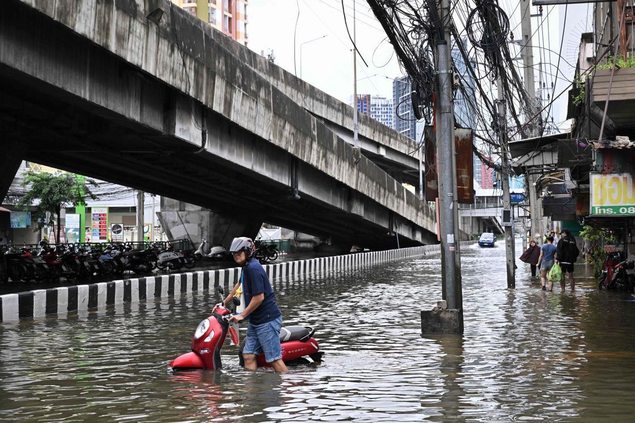 A man pushes a bike on a flooded road in Ramkhamhaeng district in Bangkok on Sept 27, 2026. Thousands of Bangkok residents awoke in shelters after flooding triggered by days of heavy rain in the Thai capital inundated homes and roads, with some starting to dry out their homes and belongings. - Photo: AFP