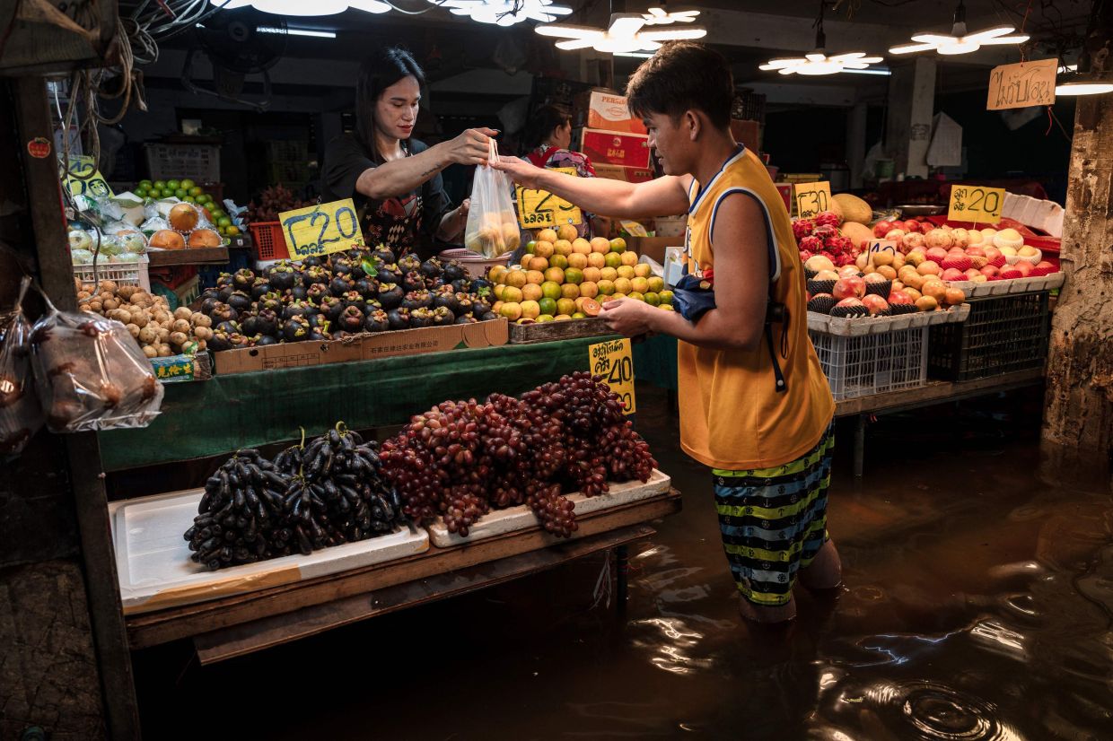 A woman sells fruit from a stall surrounded by flood waters in the Bang Kapi district of Bangkok on Sept 27, 2026. Thousands of Bangkok residents awoke in shelters on Sept 27 after flooding triggered by days of heavy rain in the Thai capital inundated homes and roads, with some starting to dry out their homes and belongings. - Photo: AFP