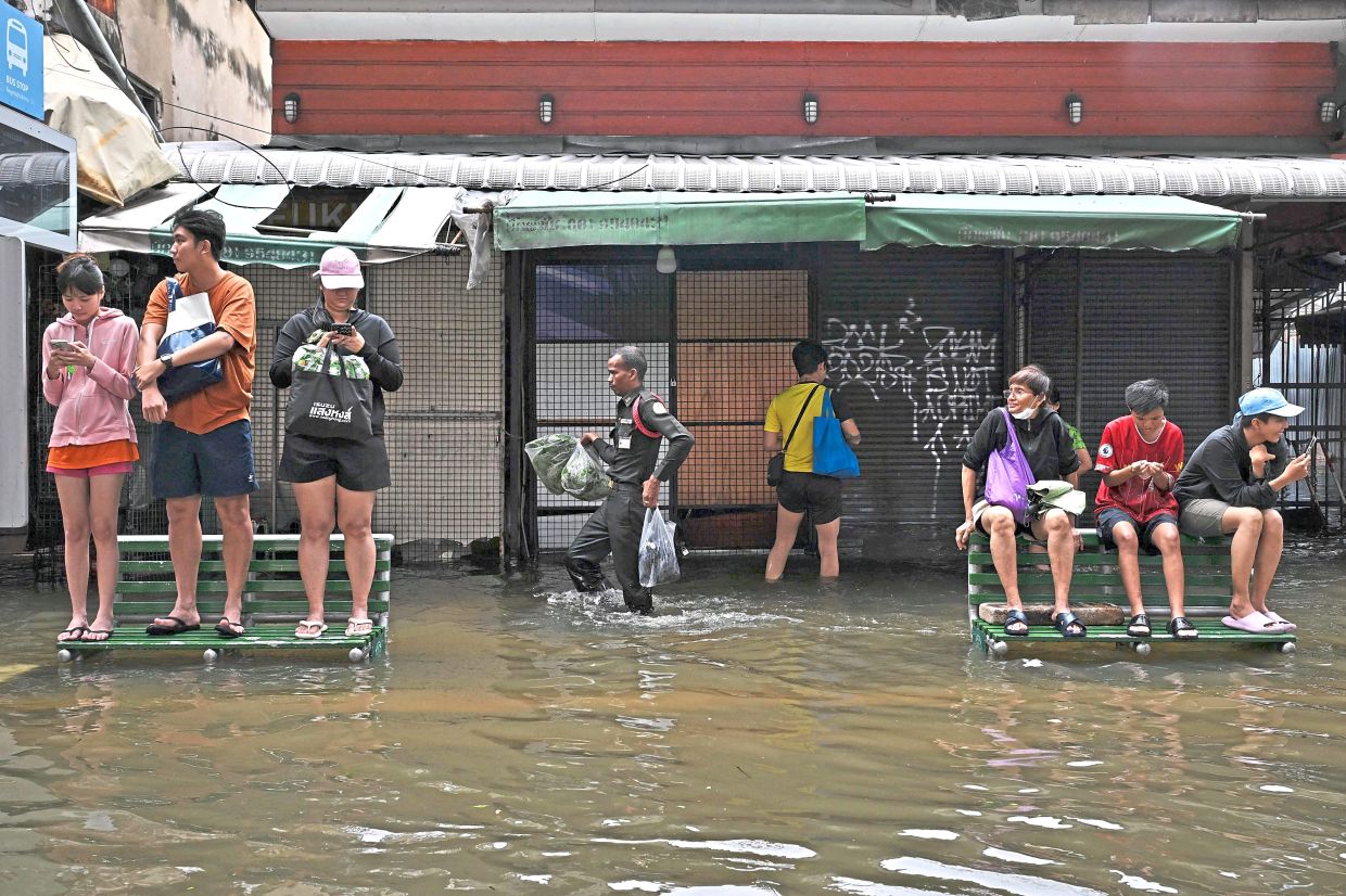 That sinking feeling: People standing on benches on a flooded pavement in Ramkhamhaeng in Bangkok. — AFP