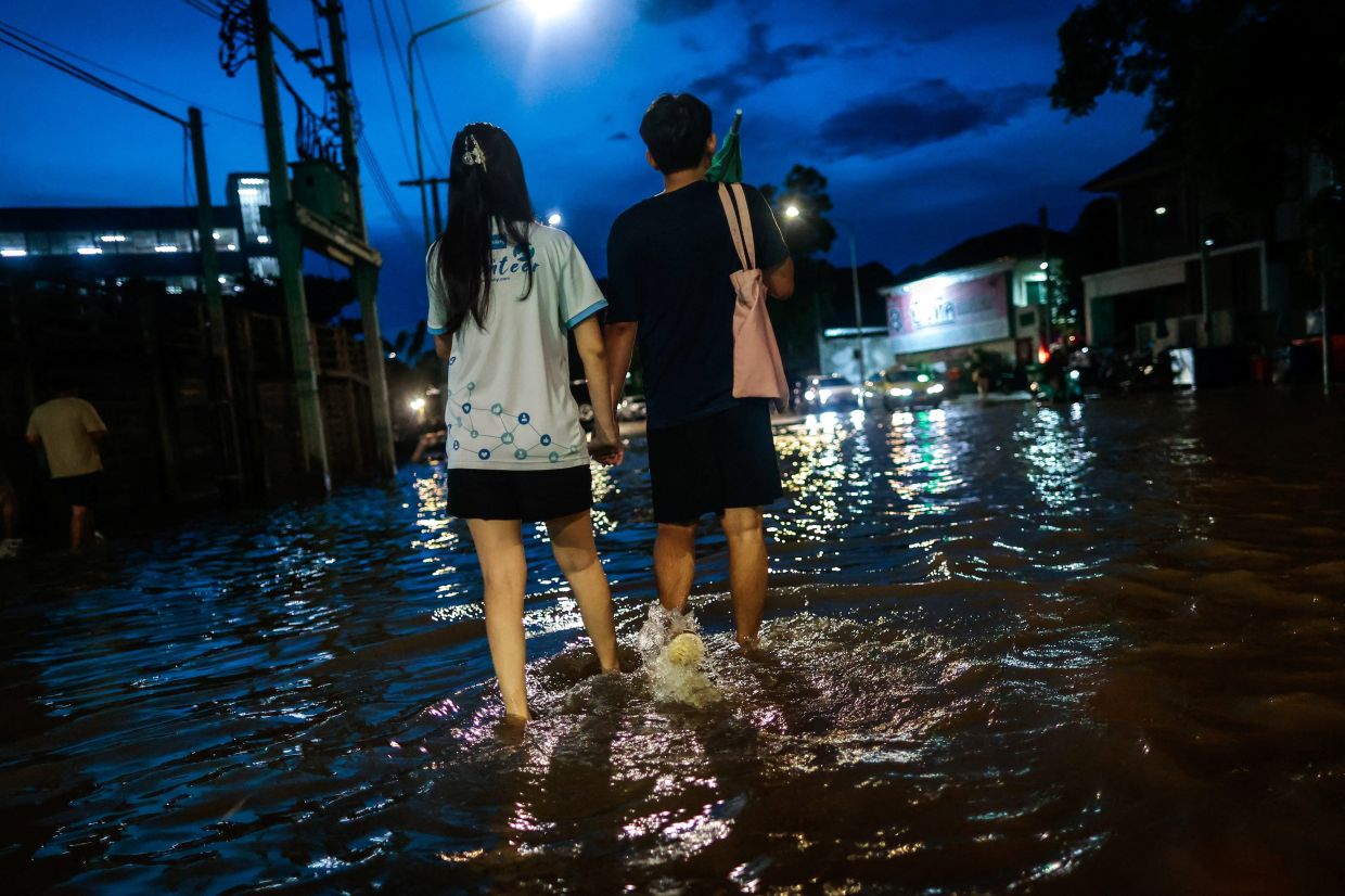 People walk as they wade through a flooded area following heavy rain in Bangkok, Thailand, on Monday, September 28, 2026. -- Photo: REUTERS/Patipat Janthong