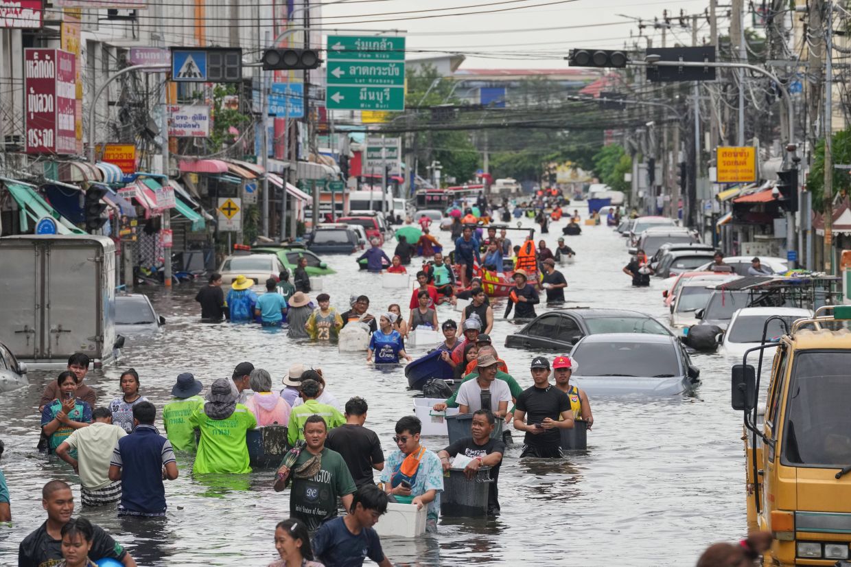 People wading through a flooded street after heavy rain in Bangkok. - AP