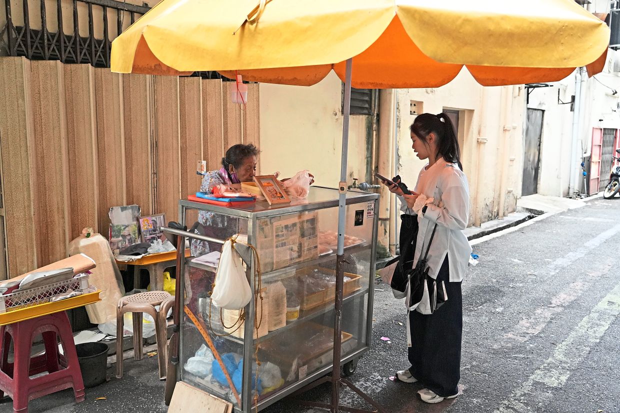 A customer buying homemade kaya pastries and Swiss roll from Wong’s pushcart stall at a lane off Jalan Yap Ah Loy.