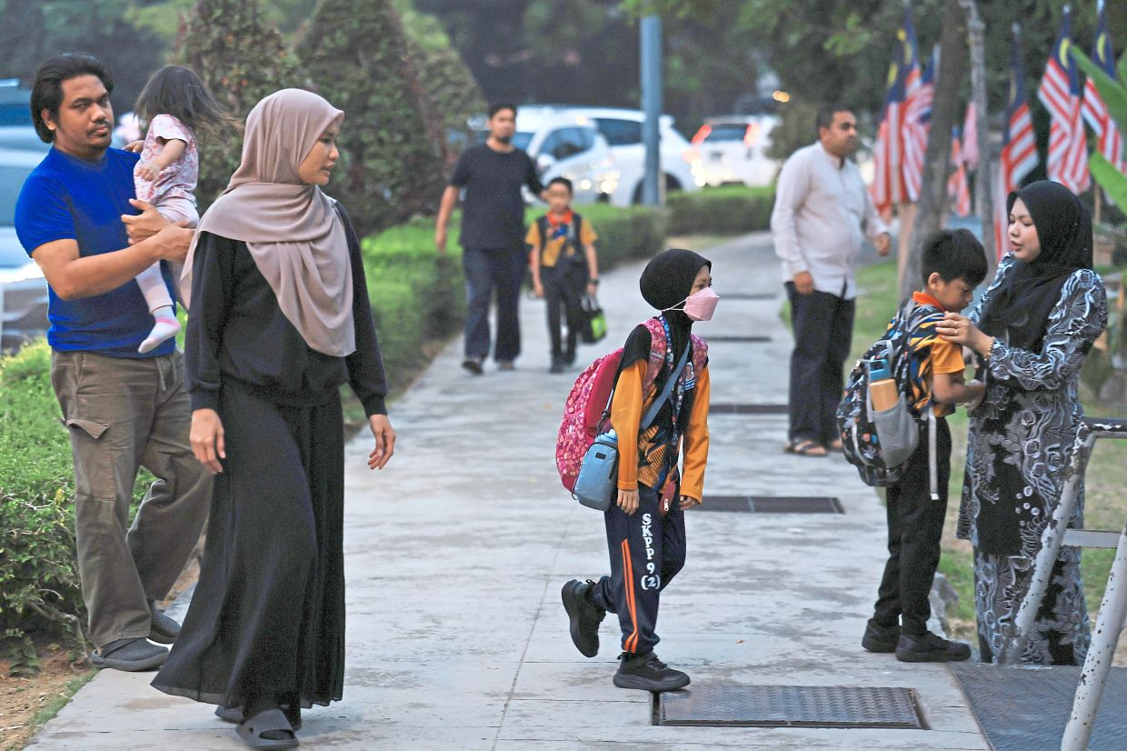 2. Parents ensuring their children are masked before entering school in Putrajaya. Schools and families are taking precautions, including wearing face masks and halting outdoor activities, as haze persists. — Bernama