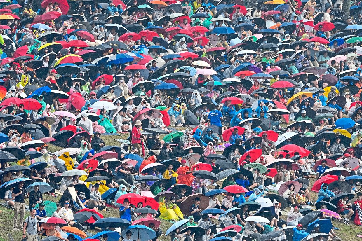 4. People sheltering under umbrellas and rain covers on a hillside at Sepang. After staying away during practice and qualifying, heavy rain swept across the circuit on race day, delaying the start and putting drivers to the test. — AP