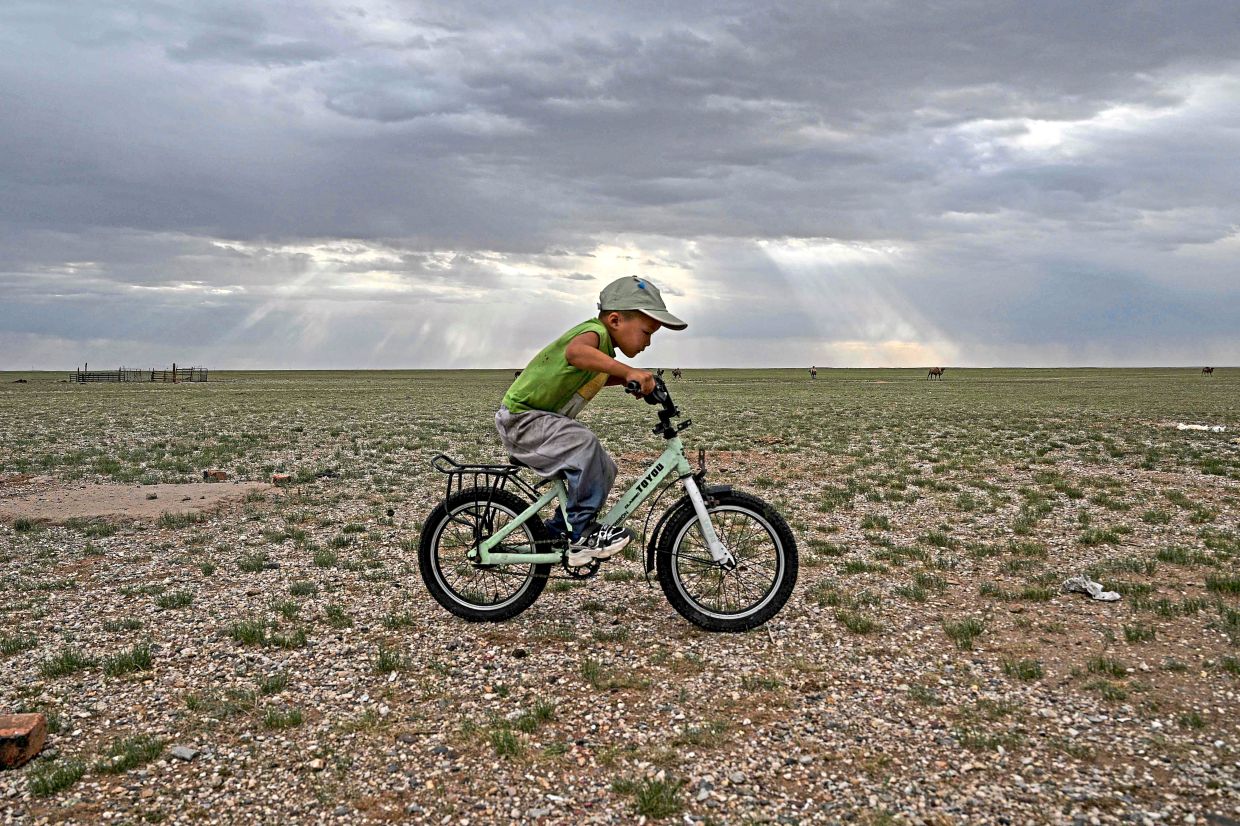 A boy rides a bicycle next to his ger, a traditional Mongolian tent.