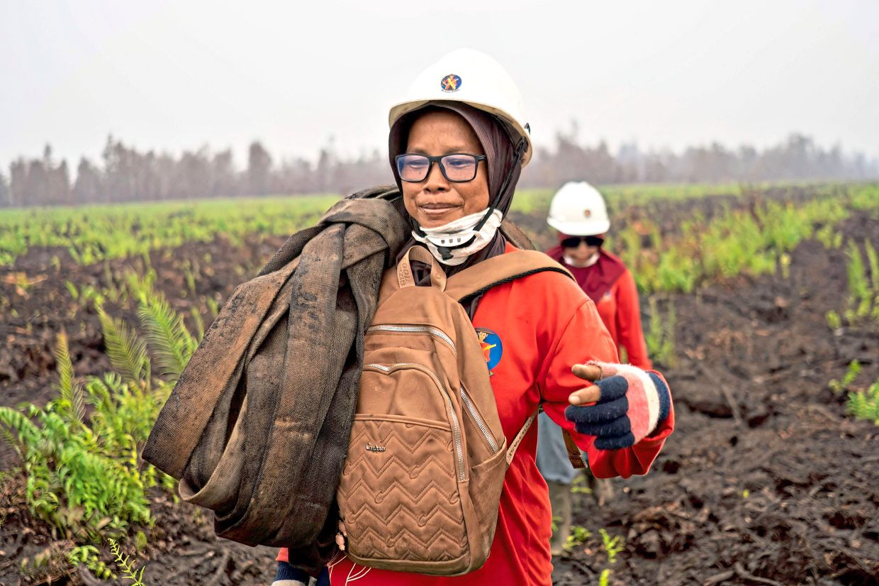 A member of the all-women The Power of Mama (TPoM) volunteer firefighting team carries a fire hose while battling smouldering peatland. Photo: Heribertus/AFP