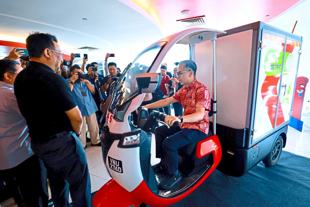 Eco-friendly delivery: Fahmi trying out Malaysia’s first electric three-wheeled motorcycle while attending the launch of the World Post Day celebration. — Bernama