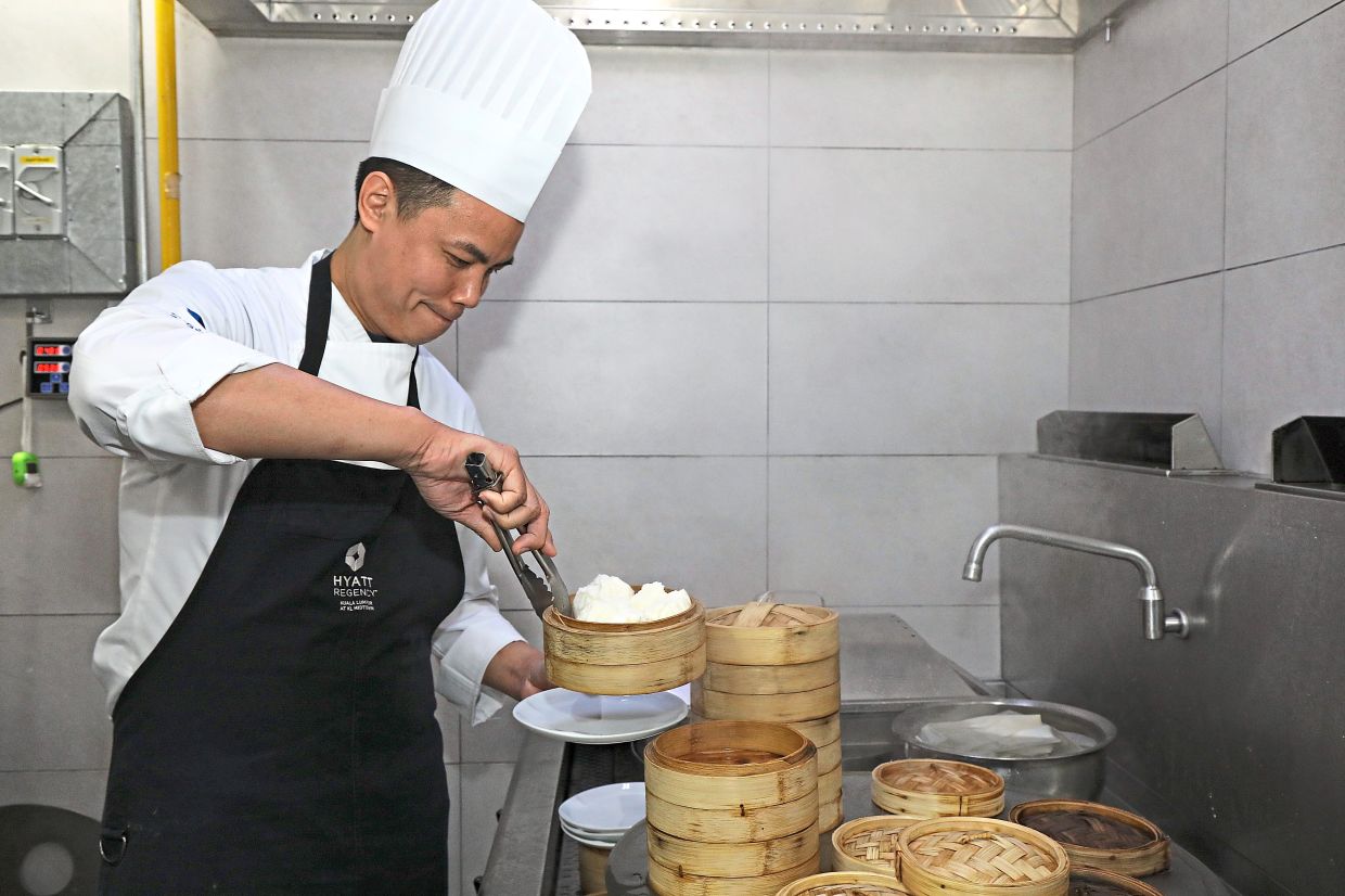 Yee gently placing the hot basket of steamed pau onto a plate.