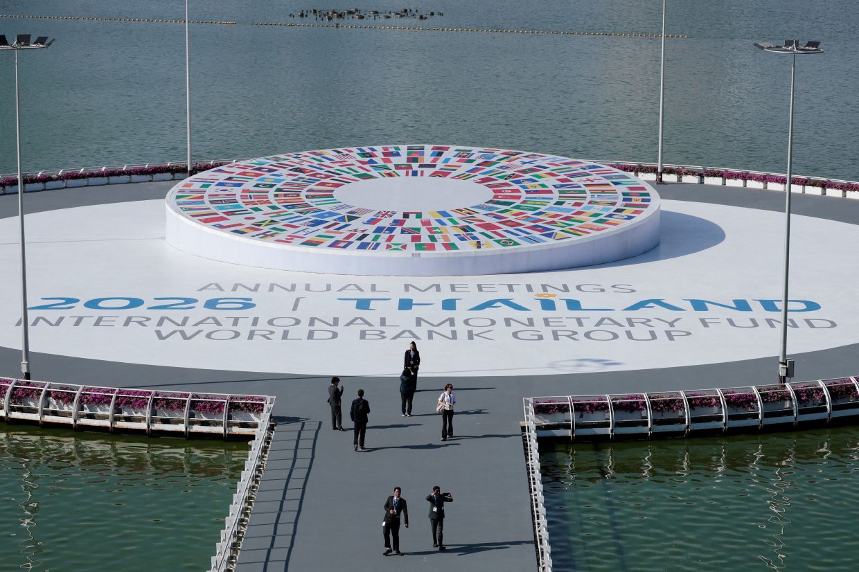 People stand next to the IMF/World Bank 2026 Annual Meetings logo at the Queen Sirikit National Convention Center (QSNCC) in Bangkok, Thailand, on Monday, October 12, 2026. -- Photo: REUTERS/Patipat Janthong