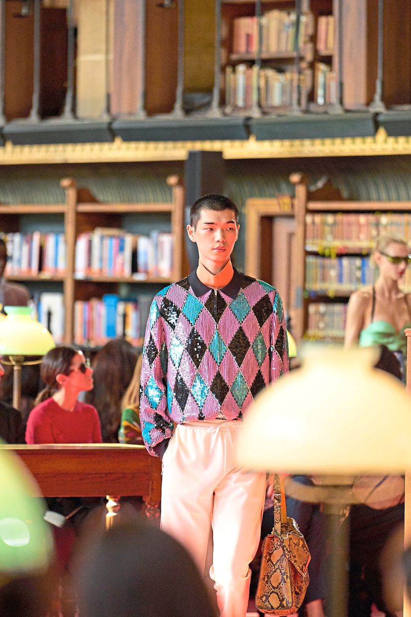 A model walks through a library as guests sit at the reading tables. Photo: Valentino