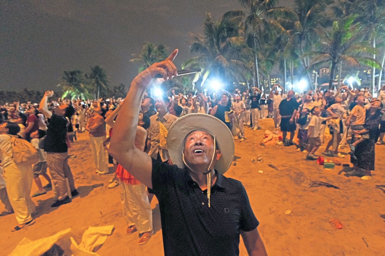 Into orbit: A man filming with his smartphone from Qishui Bay Beach during a Long March 7A rocket launch (below); and people looking at models at a souvenir store at the Wenchang Aerospace Science and Education Center, in Wenchang, Hainan province. — Reuters