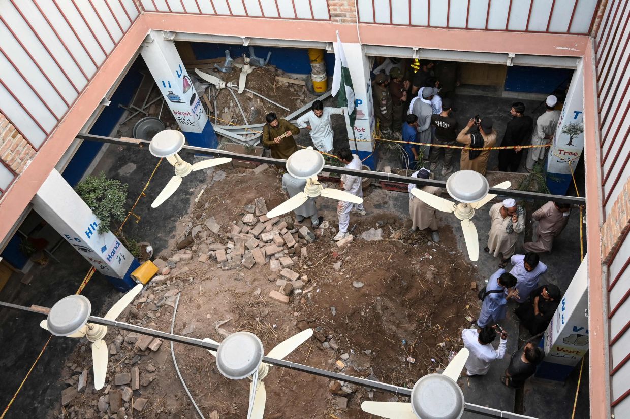 People gather around debris and rubble lying in the courtyard of a school following a roof collapse, in Peshawar on October 15, 2026. The roof of a school collapsed in Pakistan's northwestern city of Peshawar, killing a teacher and 32 students, mostly aged under 14, health officials said on October 15, as residents and rescuers scrambled to pull children from the rubble. - Photo: AFP