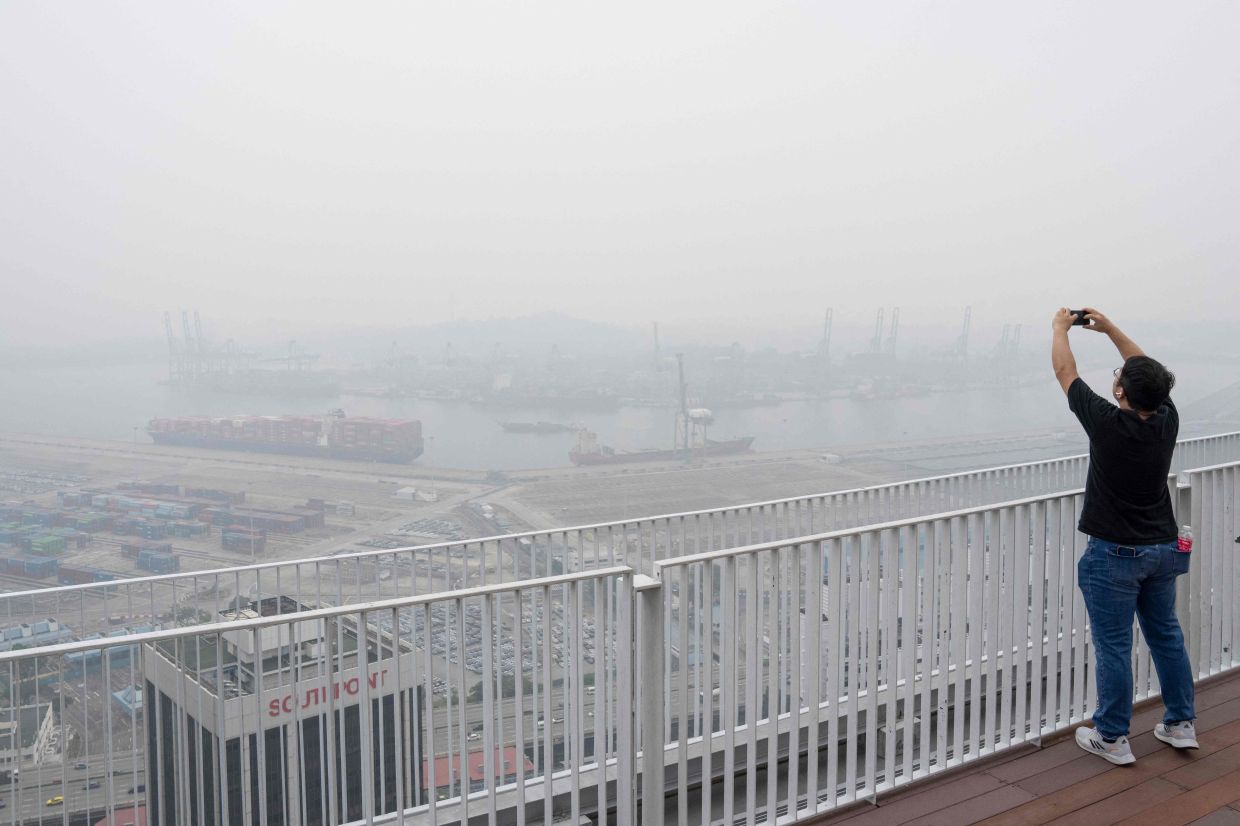 A man takes photographs from an observation deck in Singapore on Friday, October 16, 2026, as the country continues to be shrouded in haze caused by fires in Indonesia. Toxic haze has covered parts of Indonesia, Malaysia, and Singapore for weeks as Jakarta struggles to contain fires that have scorched large tracts of Borneo and Sumatra, with the smoke drifting across the region. -- Photo by Yuichi YAMAZAKI / AFP