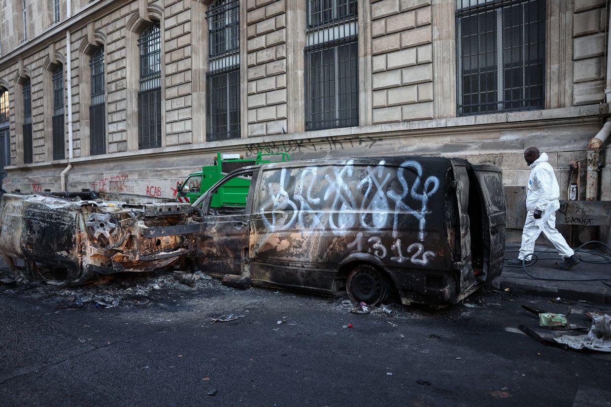 A municipal worker walks next to burnt out vehicles on a street, the day after clashes during a national day of demonstrations against the cost of living and rising fuel prices, near the Place de la Republique in Paris, France, October 18, 2026. REUTERS/Abdul Saboor