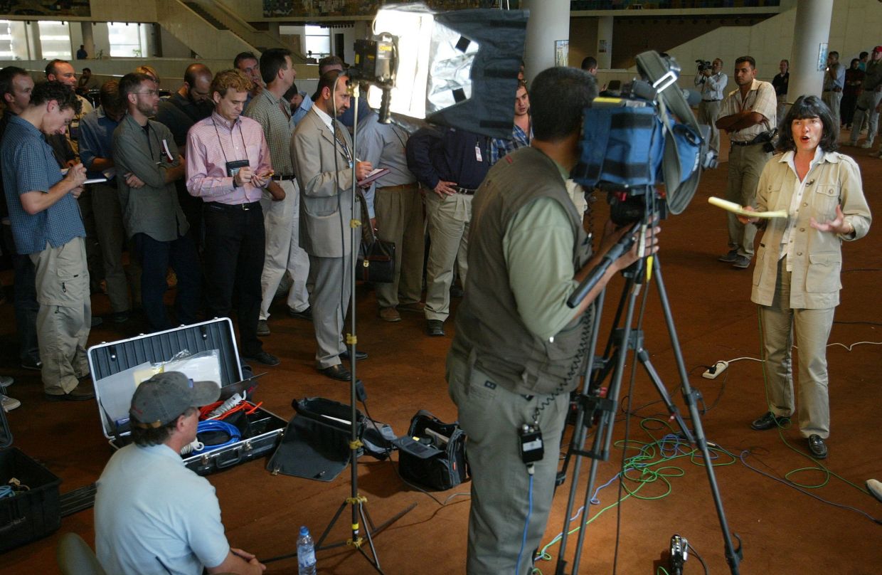 CNN correspondent Christiane Amanpour (right) makes a live broadcast while surrounded by reporters taking notes, after she managed to scoop the press pool and gain access to Saddam Hussein's court appearance July 1, 2004. Photo: Reuters