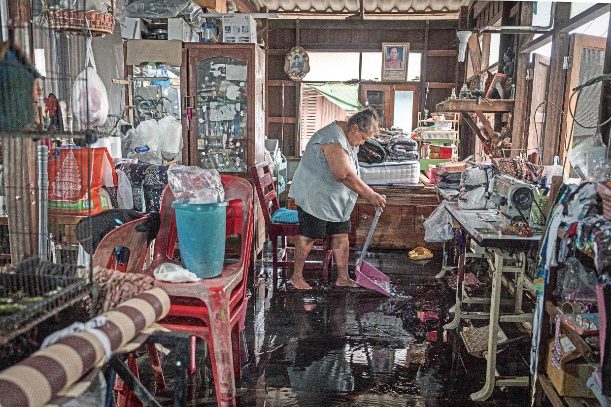 Fighting a losing battle: Yupin Nakbanlang using a dustpan to scoop floodwater from inside her home in Ayutthaya. — AFP