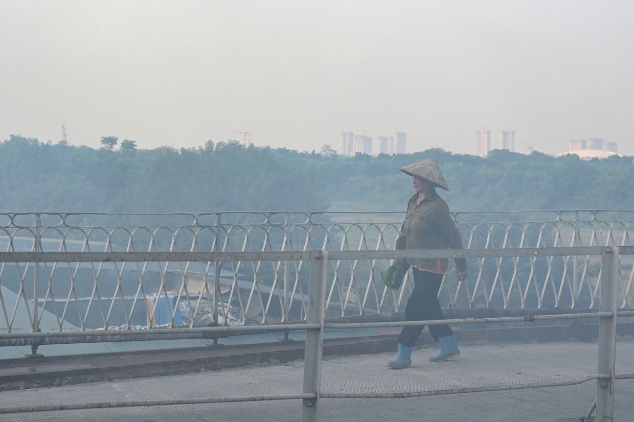 A woman walks across the Long Bien Bridge covered by haze in Hanoi on Friday, October 23, 2026. -- Photo by Nhac NGUYEN / AFP