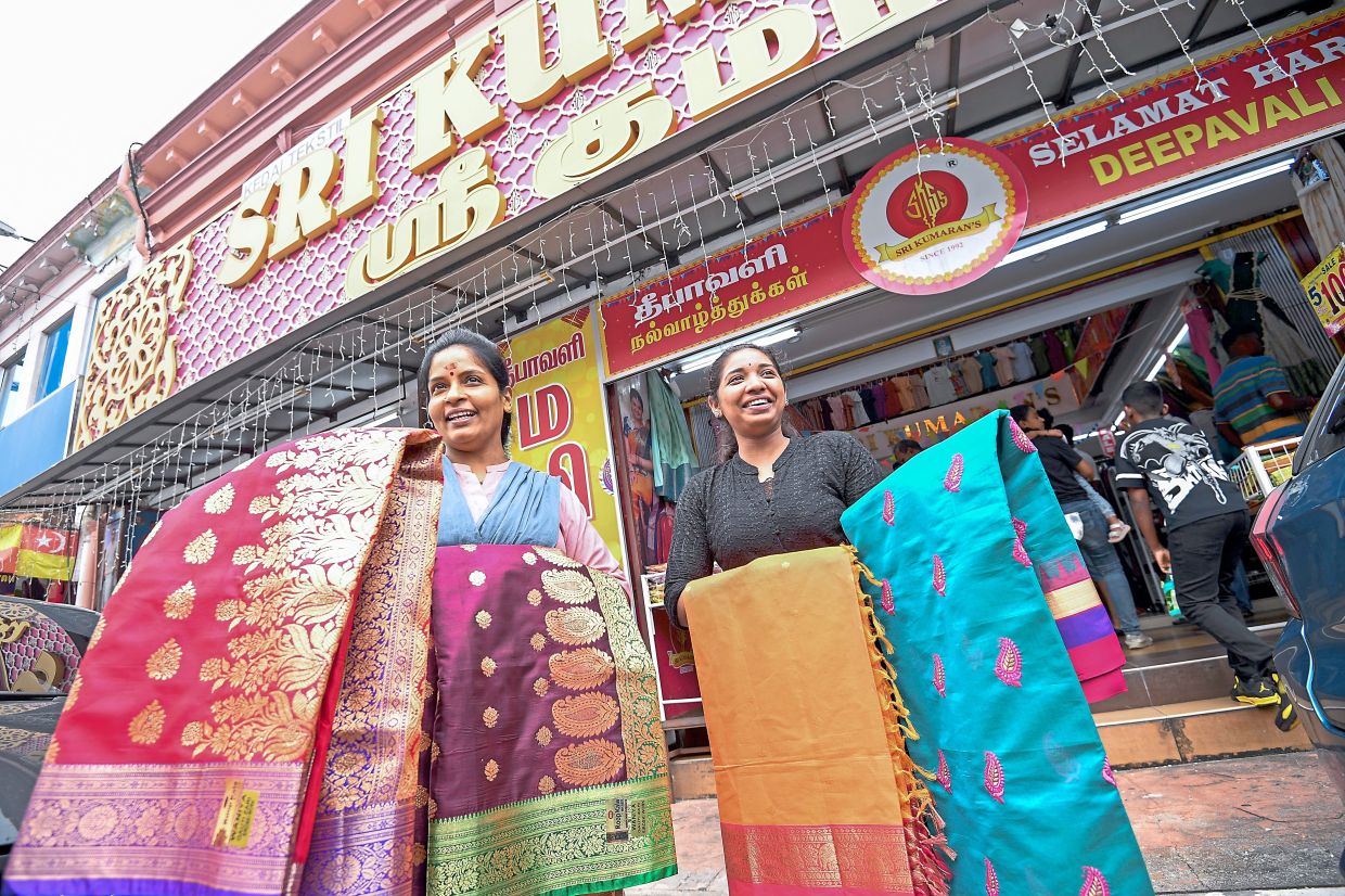 Kala Devi (left) and Shaliny drape sarees over their shoulders and arms, turning themselves into walking displays of traditional artistry as they stand along busy Jalan Tengku Kelana to attract shoppers.