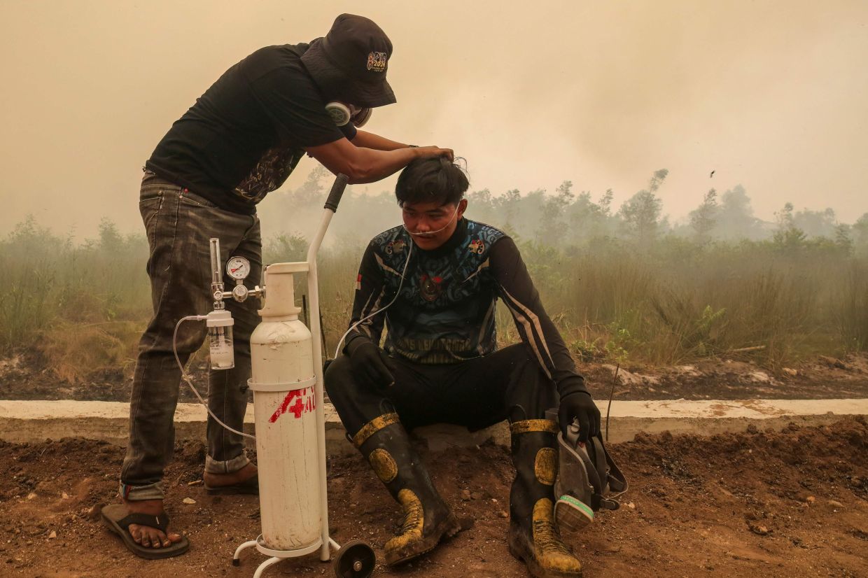 A volunteer from the Central Kalimantan Forest and Land Fire Smoke Response Coalition (RAKAT) providing mobile oxygen relief to a firefighter while battling forest and land fires in Palangkaraya, Central Kalimantan. Toxic haze has covered parts of Indonesia, Malaysia, and Singapore for weeks as Jakarta struggles to contain fires that have scorched large tracts of Borneo and Sumatra, with the smoke drifting across the region. -- Photo by REINA / AFP