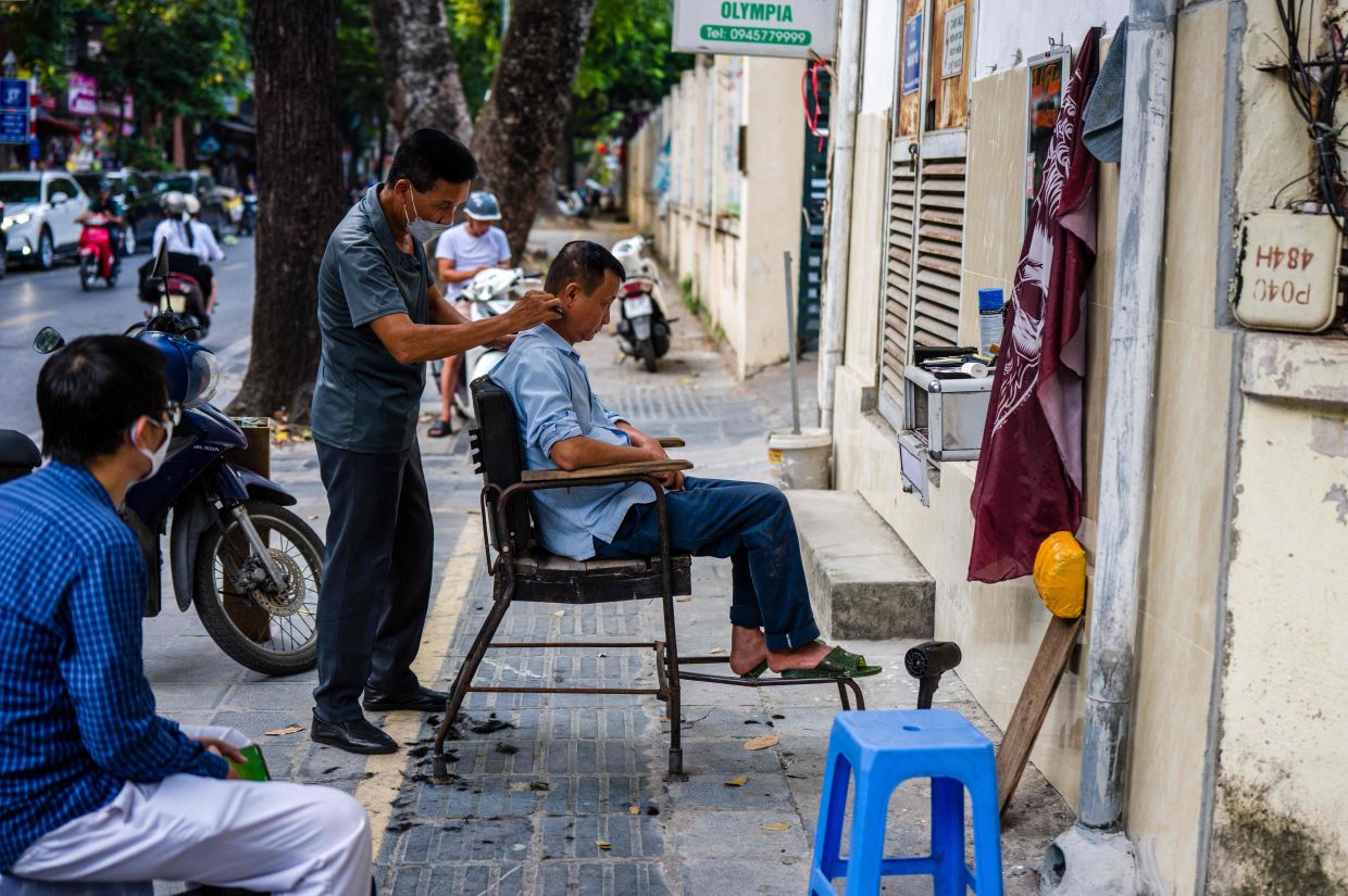A customer (left) waits while a street barber in Hanoi cuts a man's hair.-- Photo by ANTHONY WALLACE / AFP
