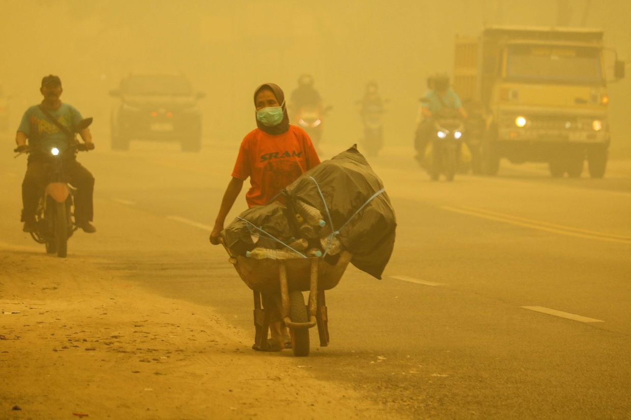 A woman wearing a face mask pushes a cart filled with used plastic bottles along a road amid thick haze from forest and land fires in the region in Palangkaraya, Central Kalimantan, on Sunday, October 25, 2026. -- Photo by REINA / AFP