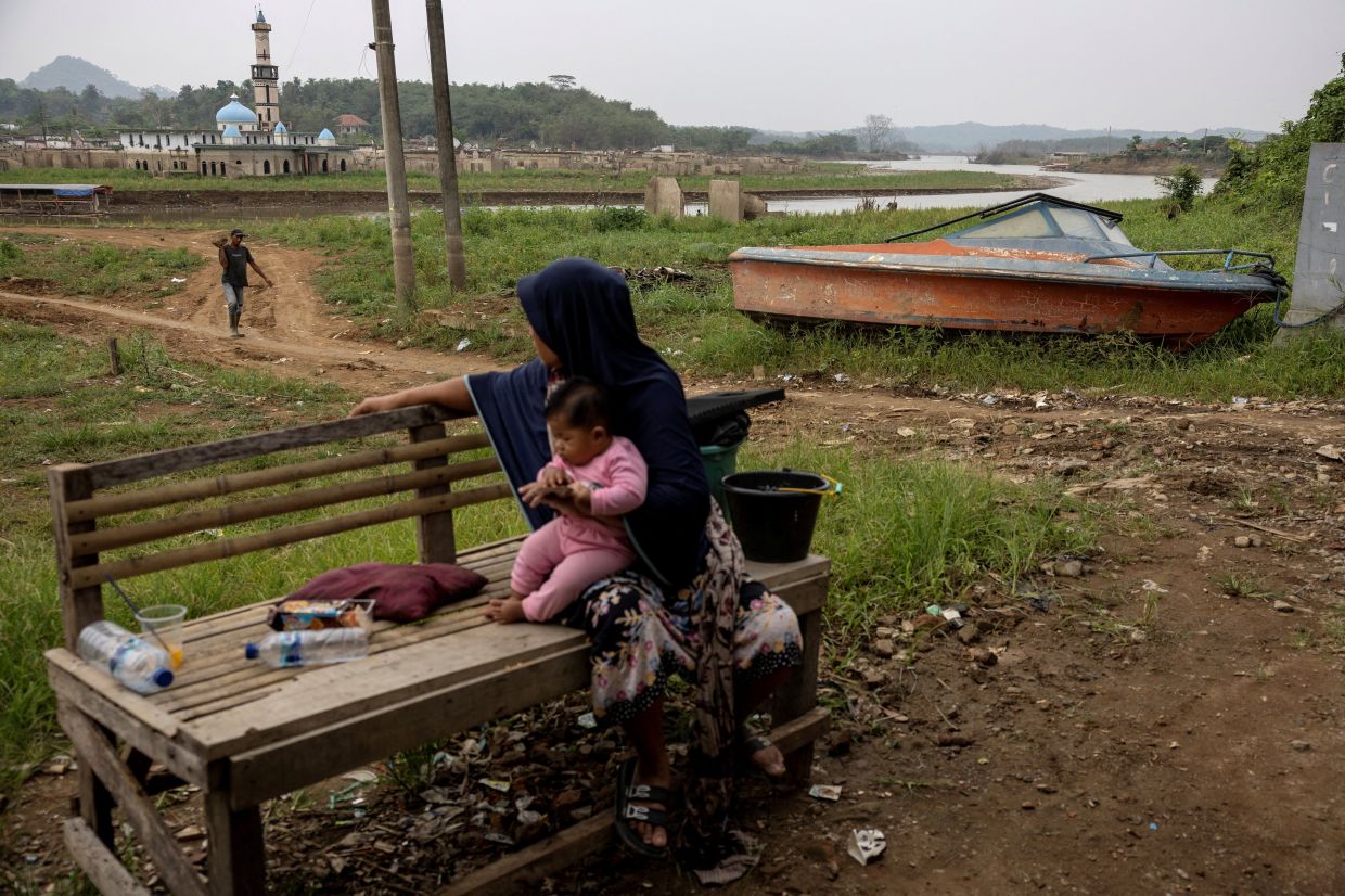 Martini, 45, holds her 6-month-old niece as they sit near a boat that is stranded in the mud after the water levels in Karian reservoir, which supplies water for surrounding areas including Jakarta, dropped amid the El Niño-driven prolonged drought, causing the remnants of the houses and mosque of the Somang village to reemerge in Lebak, Banten province, Indonesia. -- Photo: REUTERS/Willy Kurniawan