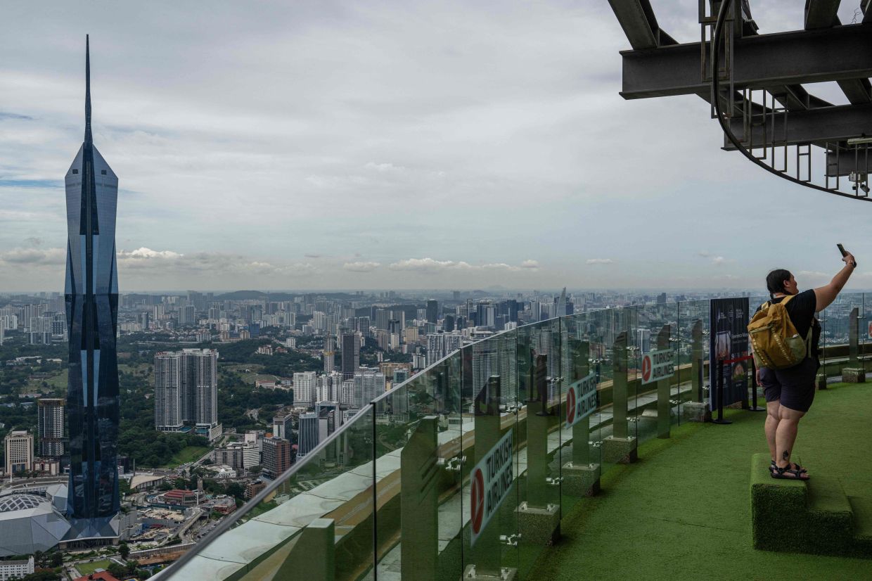 A tourist takes a selfie with the city skyline seen in the background as haze conditions due to Indonesian wildfires improve in Kuala Lumpur on Monday, October 26, 2026. The haze has sent air pollution levels surging to dangerous levels not only in Indonesia but also in Malaysia, Singapore, and East Timor, prompting the ASEAN regional bloc to call a meeting over the crisis. -- Photo by Mohd Rasfan / AFP