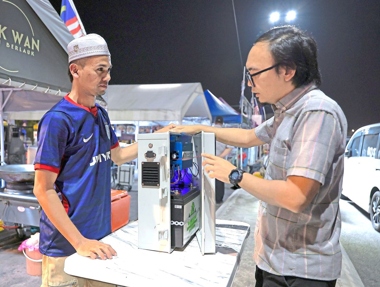 Nur Faizal (right) checking on a power inverter used by a trader at the Taman Pulai Indah night market in Iskandar Puteri.