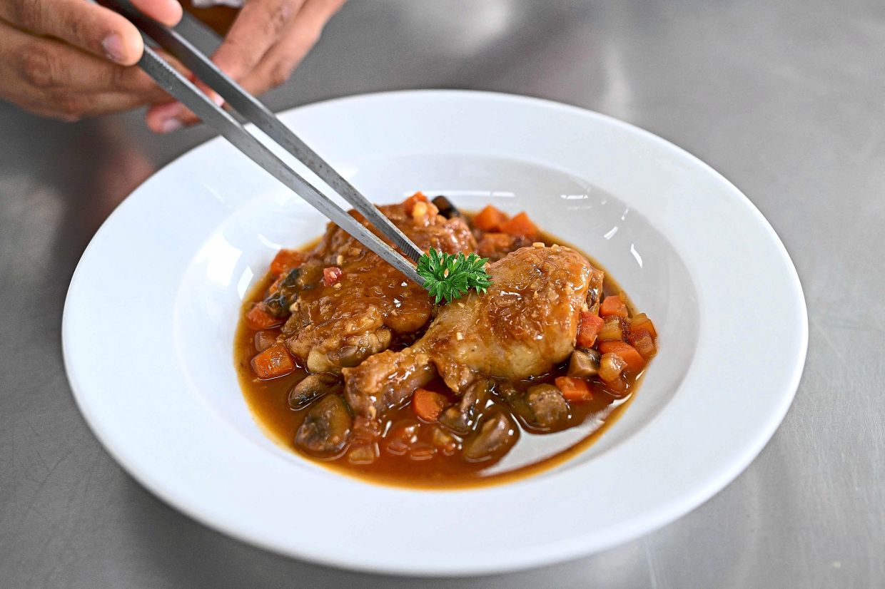 Garnishing a plate of classic French chicken dish – ‘poulet saute chasseur’. — AFP