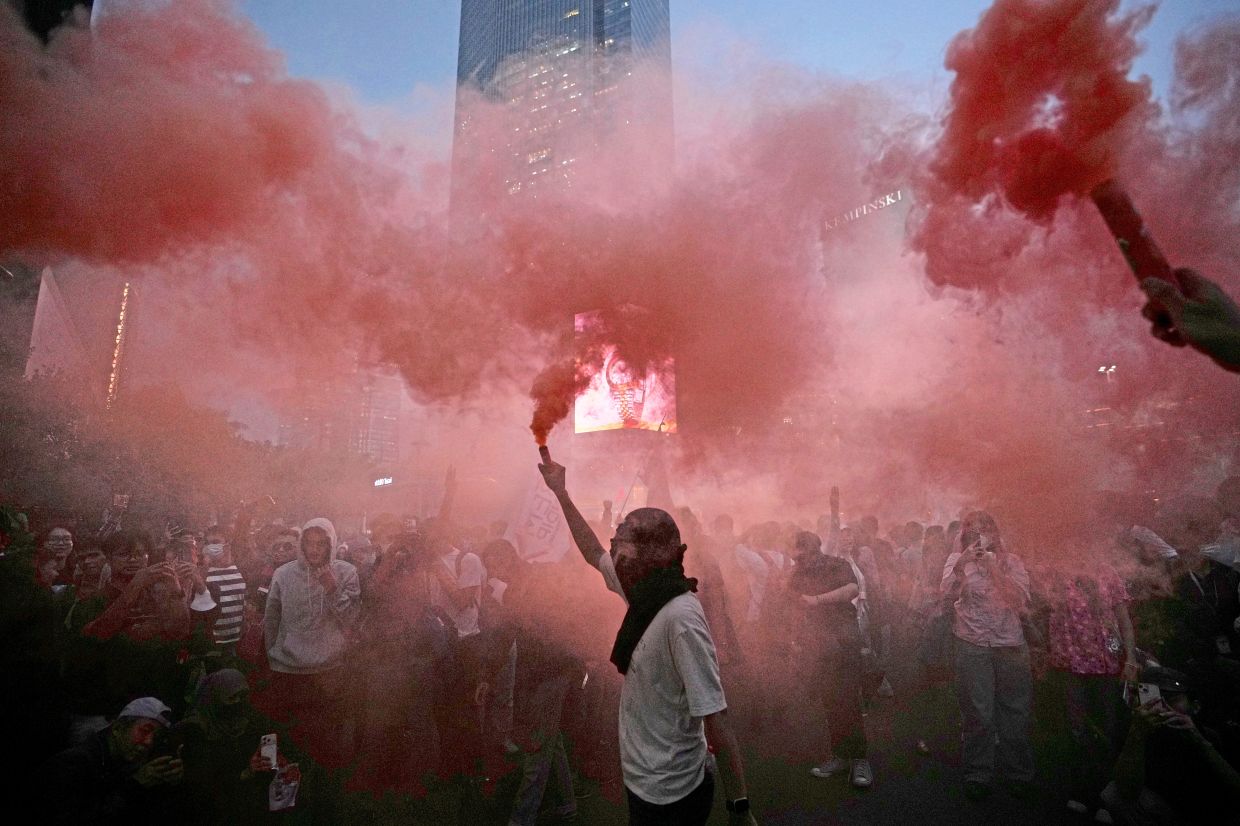 Protesters lighting up flares during a rally marking the second year since Prabowo took office. — AFP/AP/Reuters